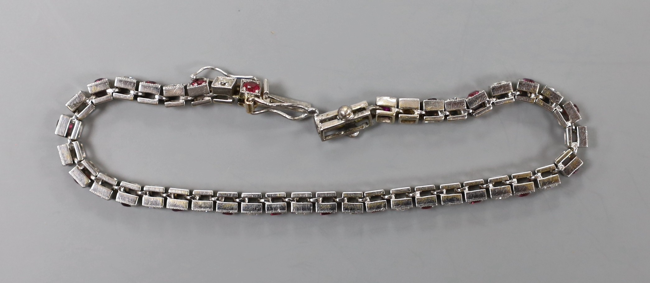 A modern white metal, twenty one stone ruby and twenty three stone diamond set line bracelet, 17.3cm, gross weight 12.5 grams.